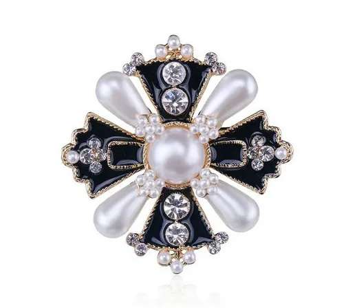 Schmuckbrosche in Form eines schwarzen Kreuzes und goldenen Perlmuttperlen.